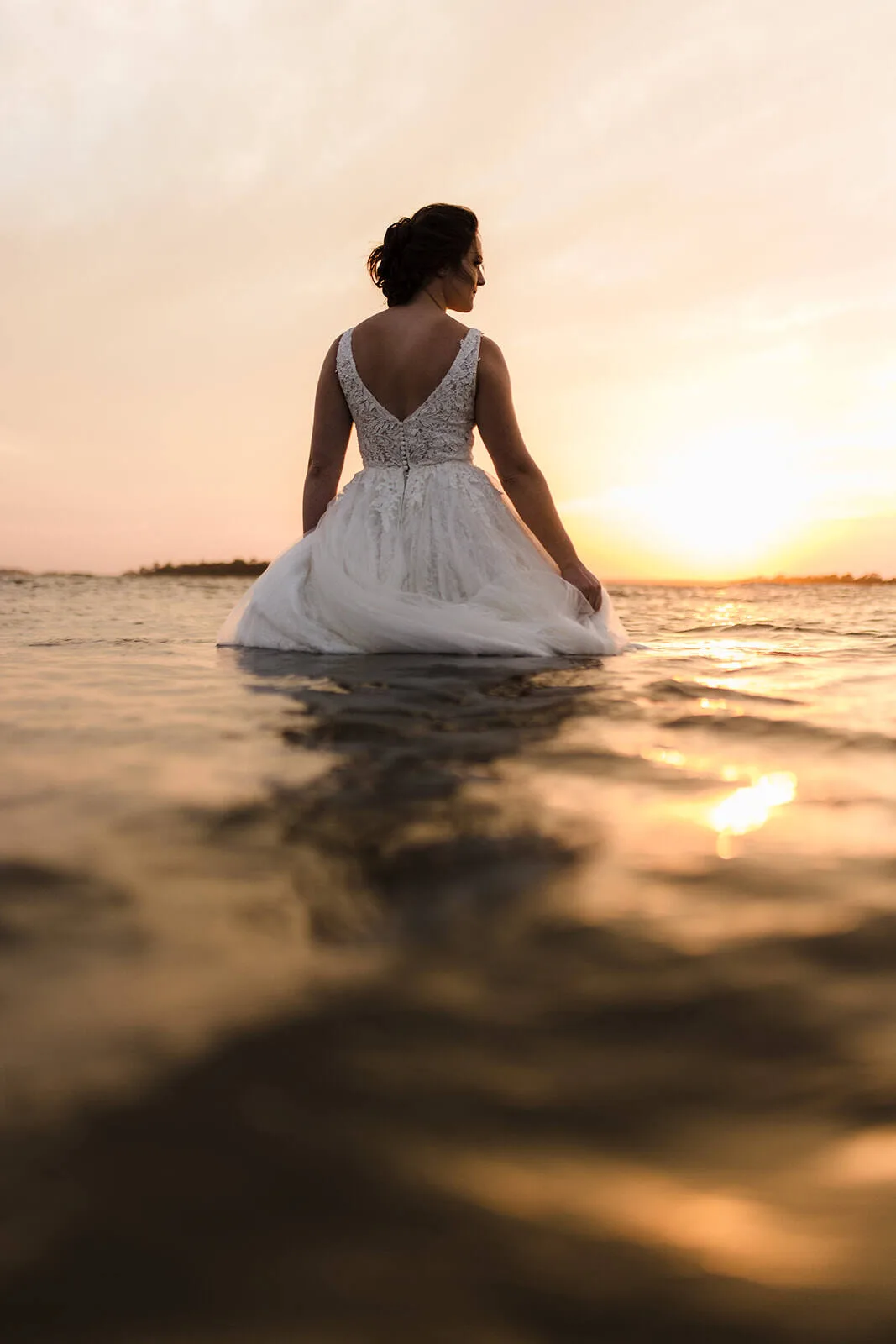 Bride standing in water at sunset